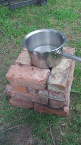 Completed project with a pot on top of the brick rocket stove surrounded by grass.