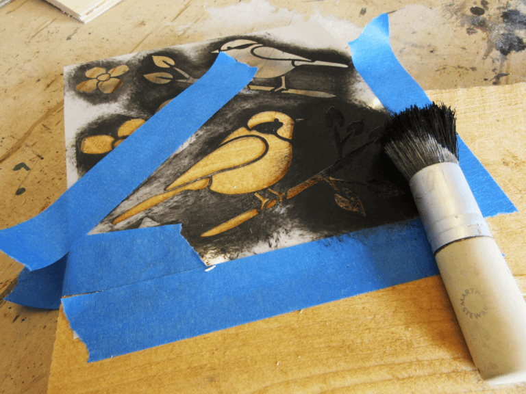 Using painter's tape while painting wooden signs with bird stencil.