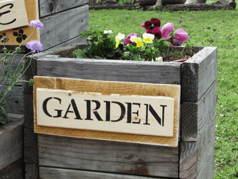 Wooden sign that has been stenciled with worde Garden and is attached to a garden planter box.